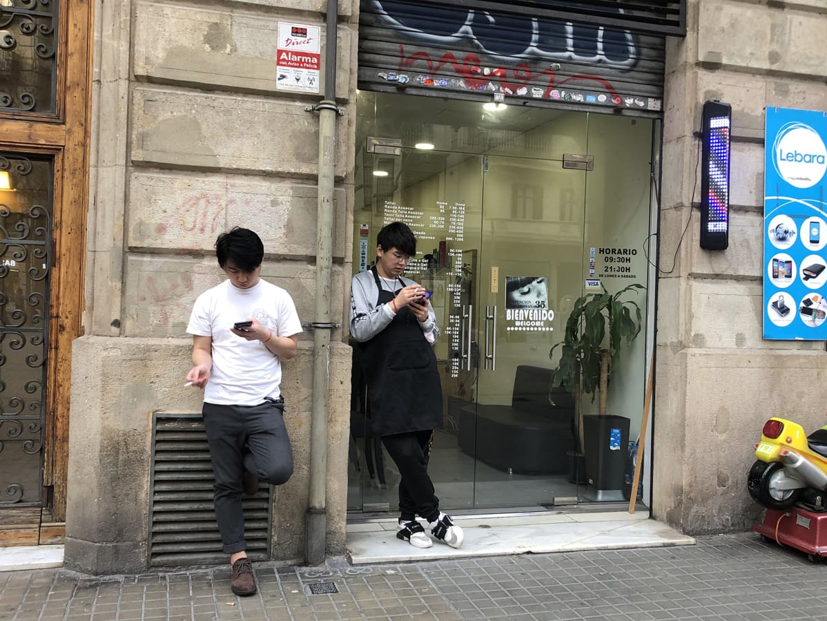 Barcelonassa kiinalaiset kynsihoitajat tupakoivat liikkeen edessä hiljaisena päivänä.