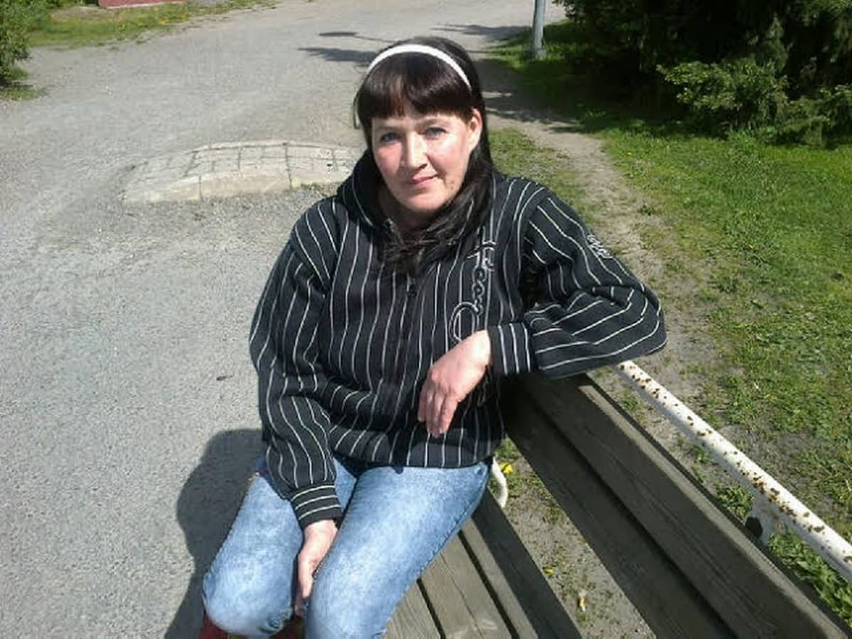 Nainen istuu puiston penkillä ja katsoo kameraan.