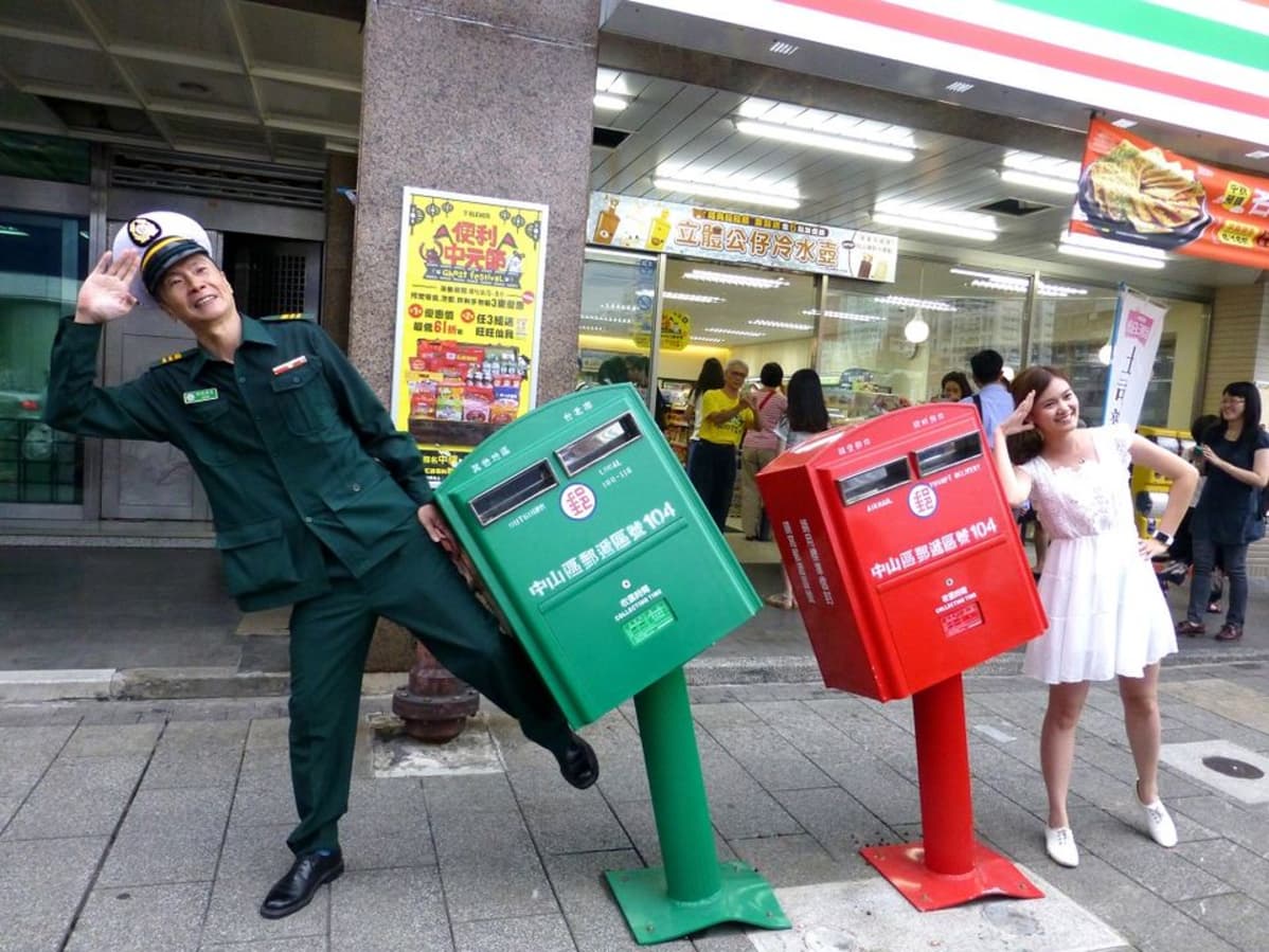 Taiwanilainen postimies poseeraa naisen kanssa kuvaa varten taifuuni Soudelorin vahingoittamien postilaatikoiden vierellä.