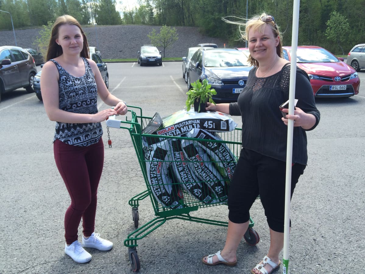 Nuori nainen ja hänen äitinsä ostosten kera tamperelaisen marketin parkkipaikalla.