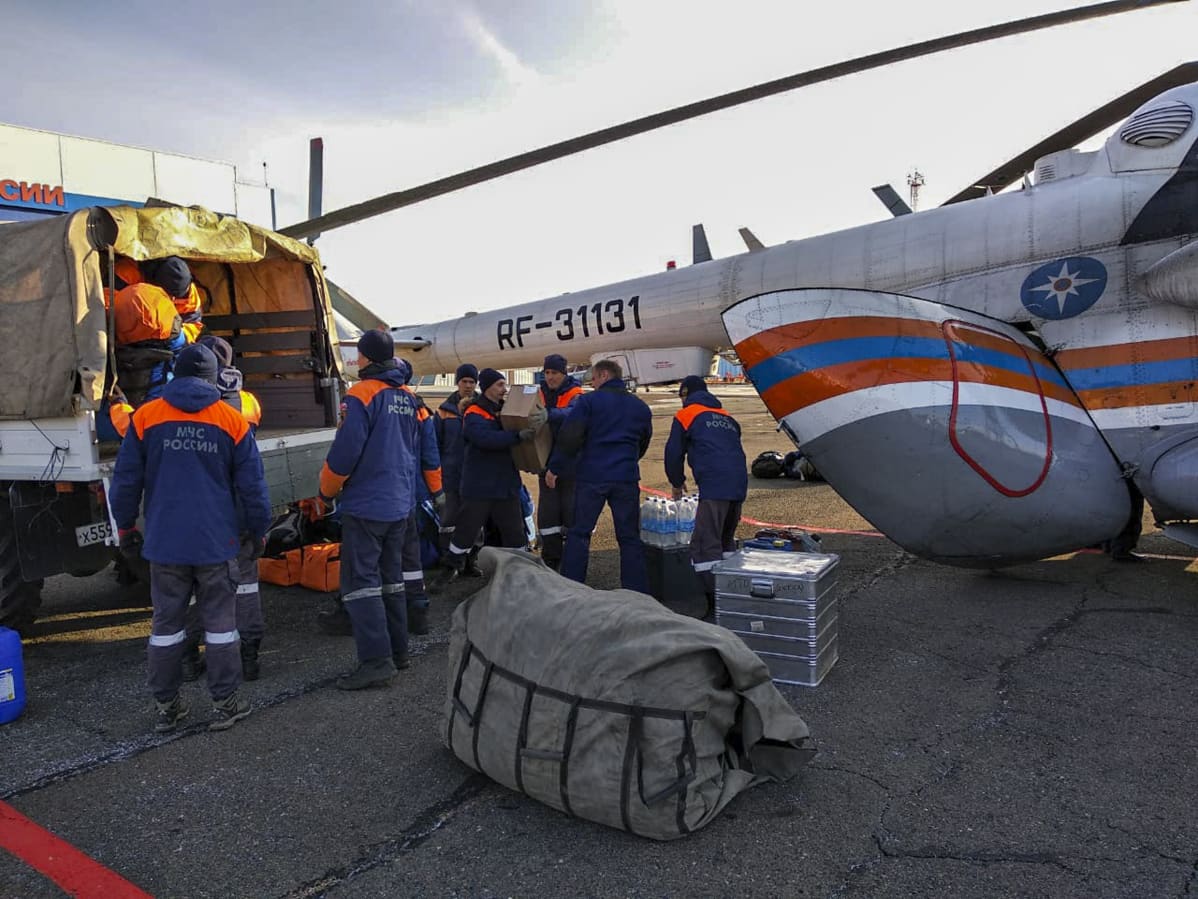 Pelastustyöntekijät lastaavat tarvikkeita. Taustalla helikopteri.
