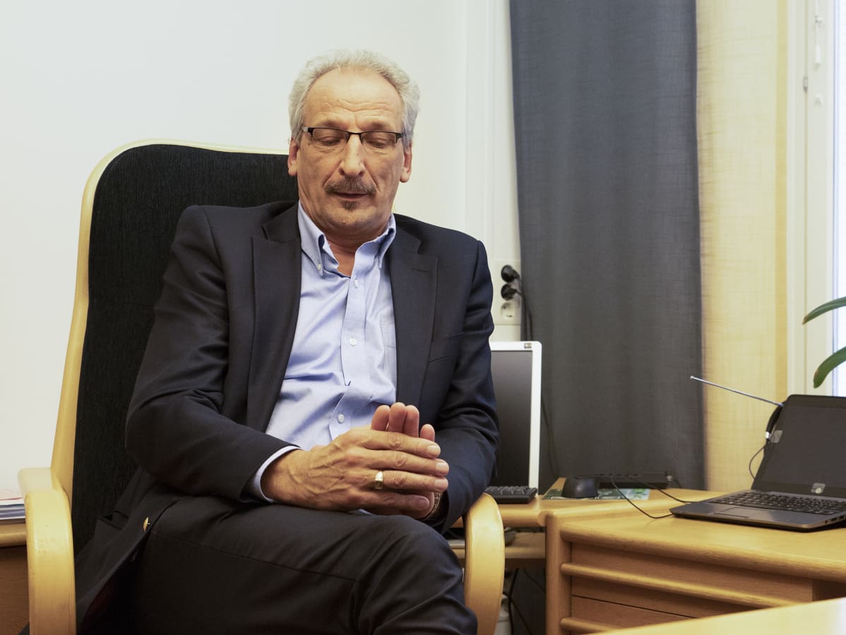 Keski-Suomen sairaanhoitopiirin johtaja Juha Kinnunen istuu työhuoneessaan ja katselee käsiinsä hieman hymyillen.
