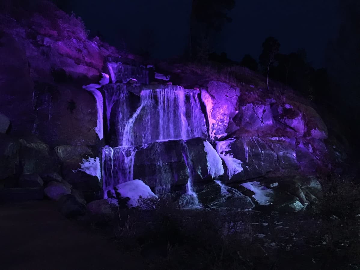 Violetilla sävyllä valaistu putouskallio Kotkan Sapokan vesipuistossa.