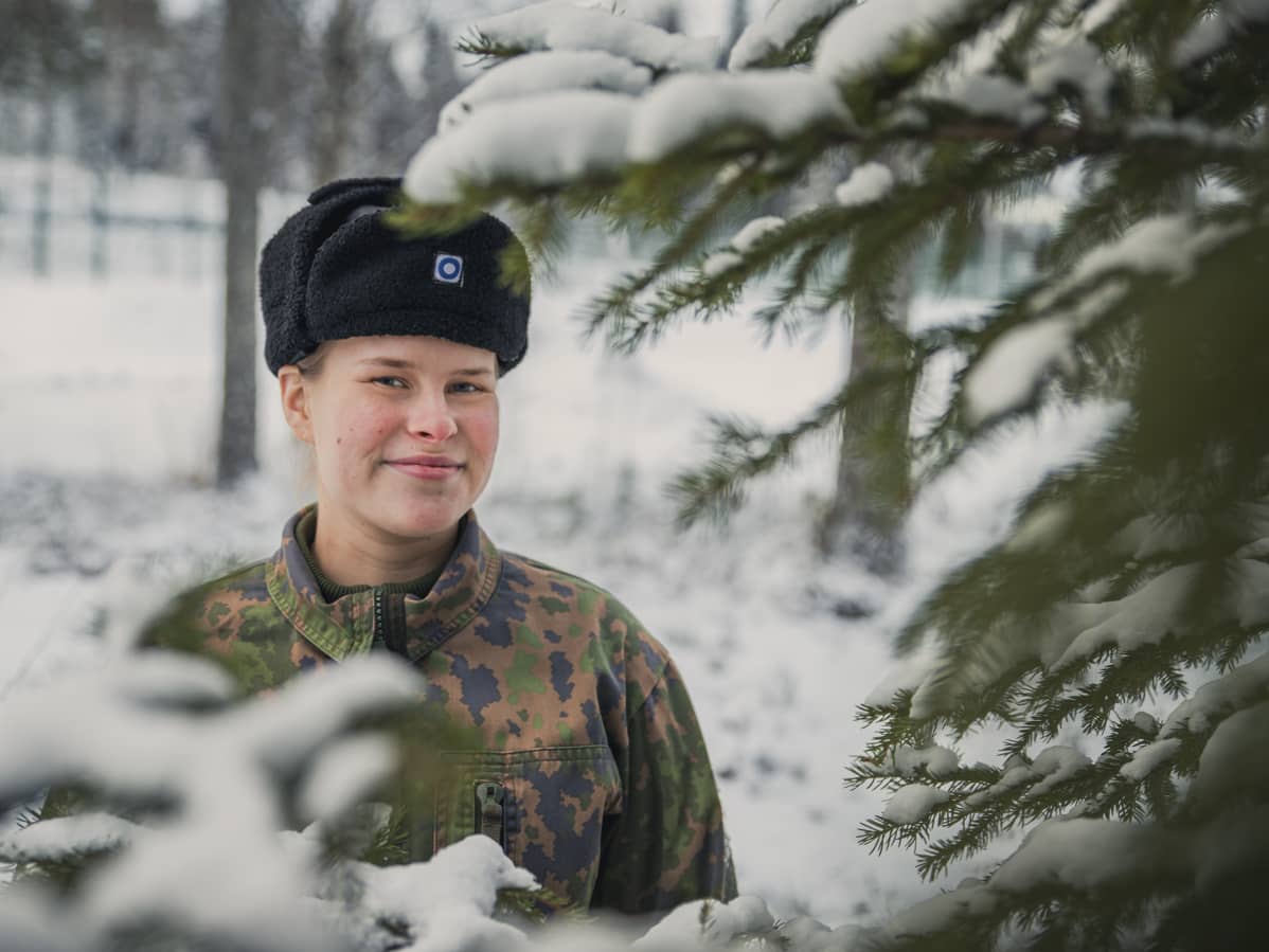 Varusmies hymyilee karvalakki päässä ulkona.