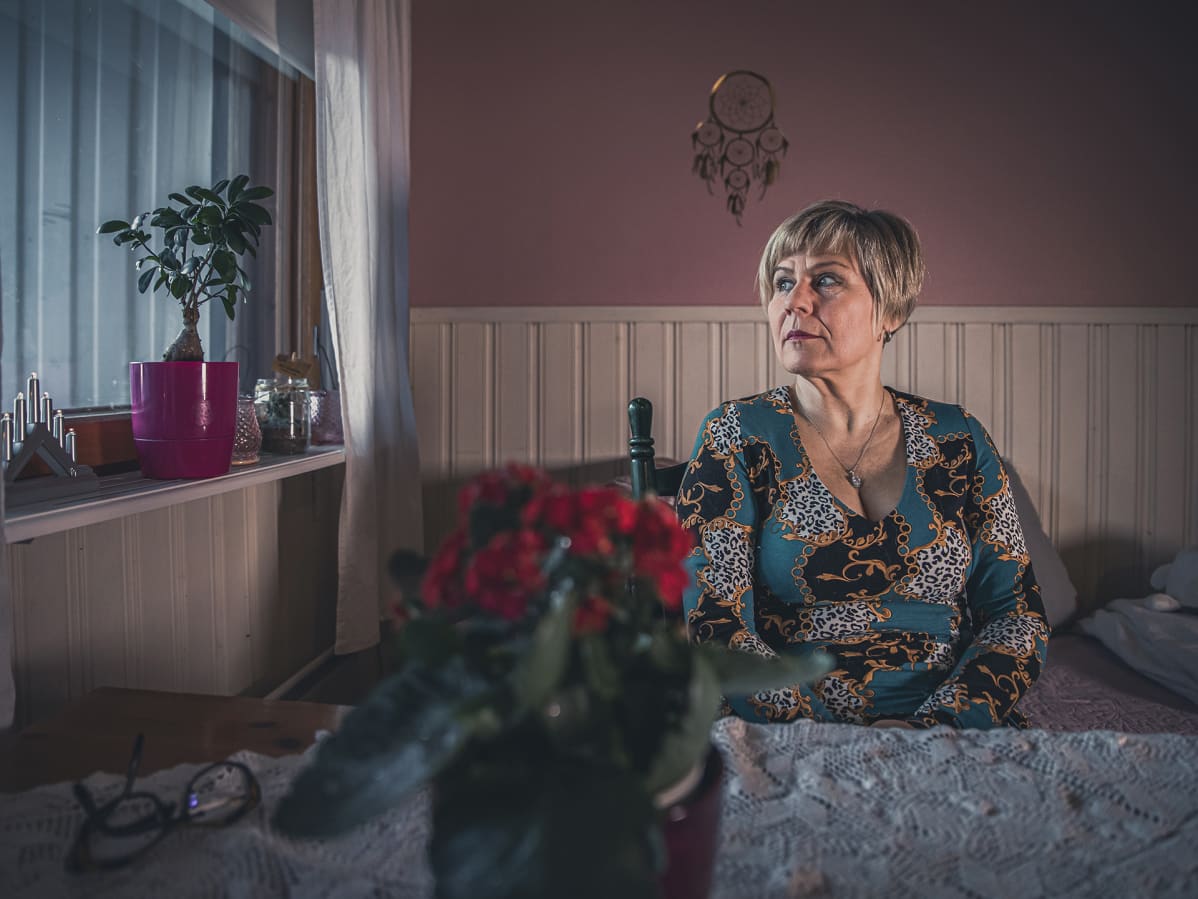 Päivi Varakas istuu keittiön pöydän ääressä vihreä mekko päällään ja katselee kuvassa vasemmalle ikkunasta ulos.