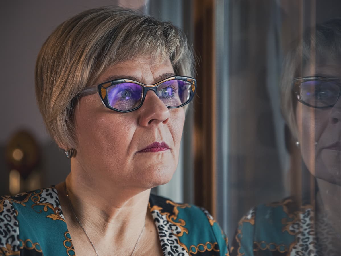 Päivi Varakas katselee ulos kotinsa ikkunasta vakava ilme kasvoillaan.