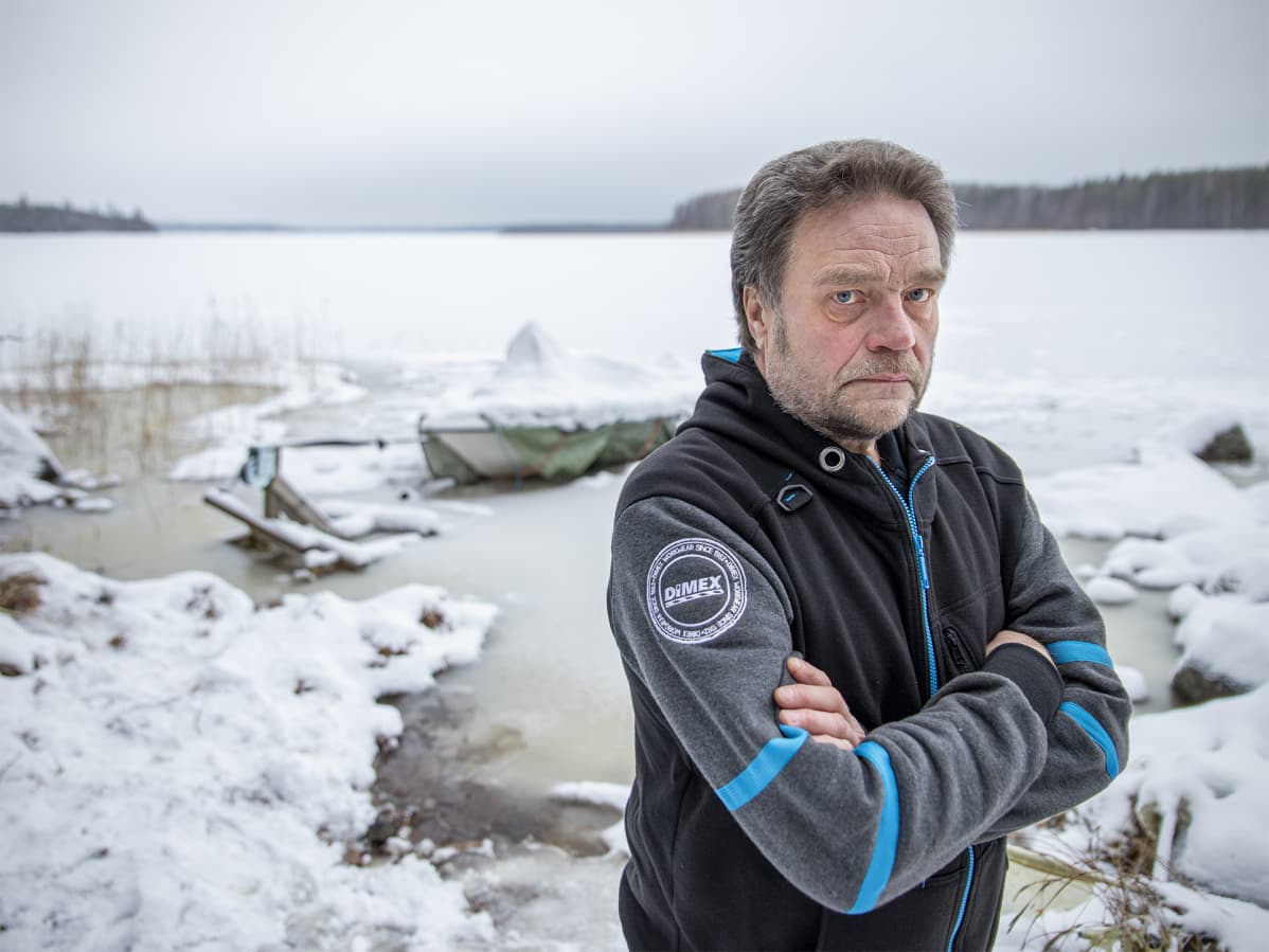 Jukka Hallberg katsoo kameraan. Taustalla veteen kiinni jäätynyt vene.