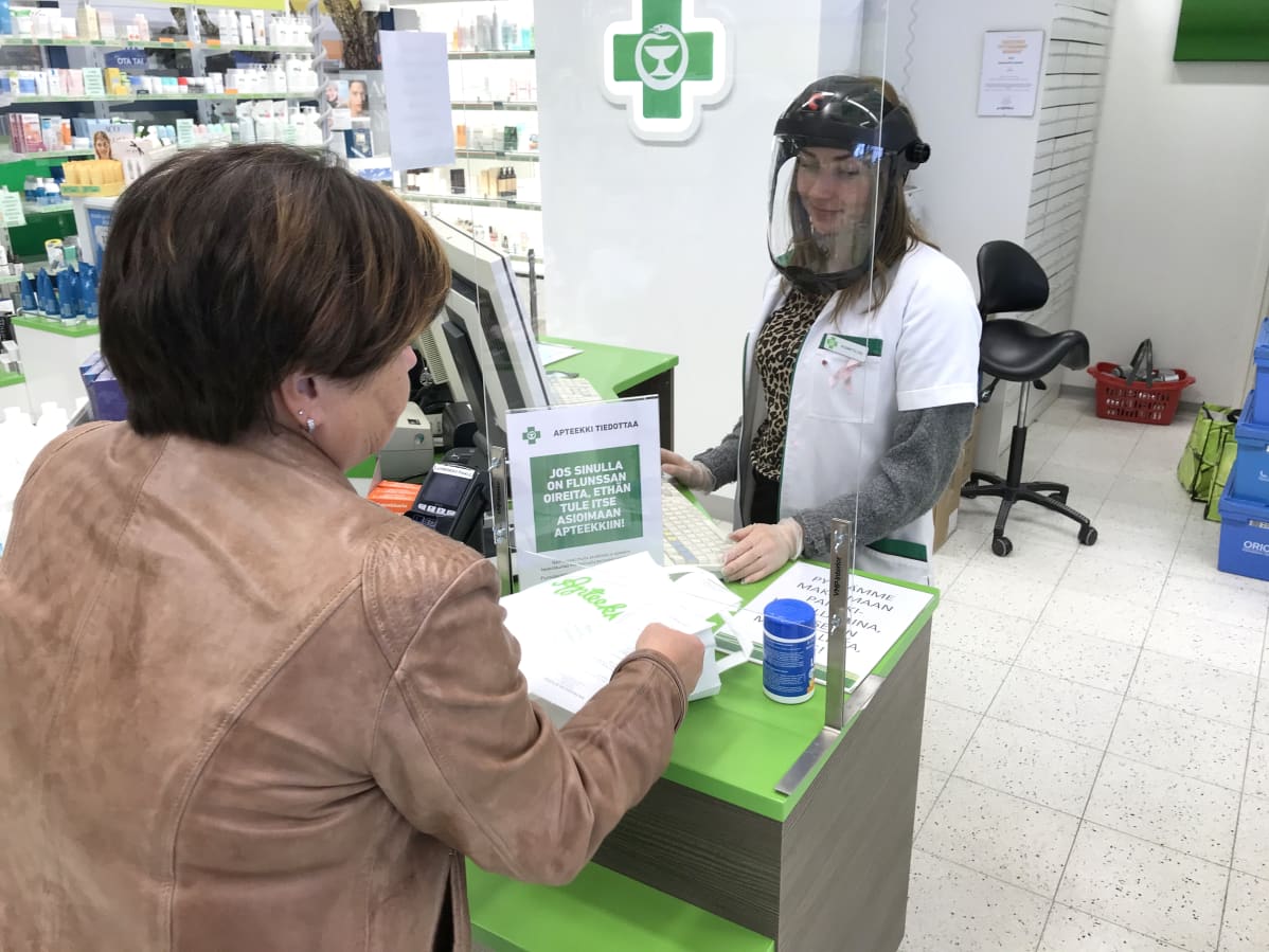 Asiakas ja suojavisiiriä pitävä myyjä Salpausselän apteekissa Lahdessa.