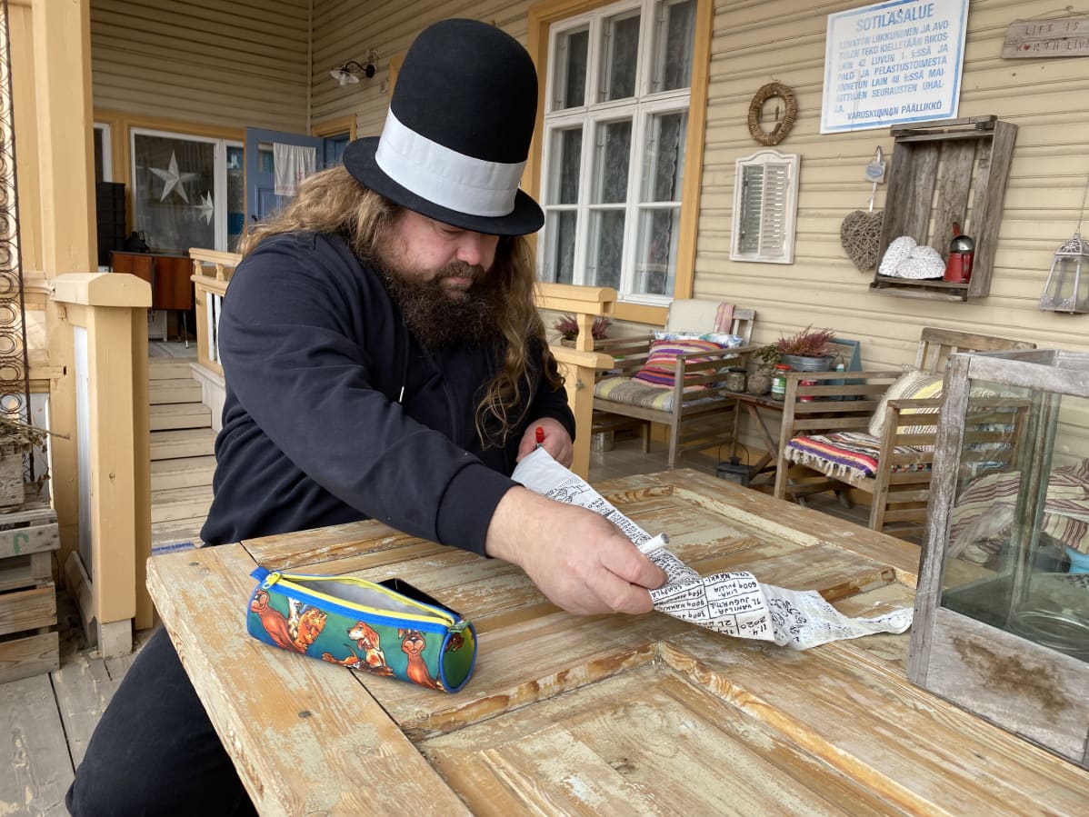 Petteri Tikkanen suoristaa vessapaperirullalle piirrettyä sarjakuvaa pöydän ääressä terassilla.