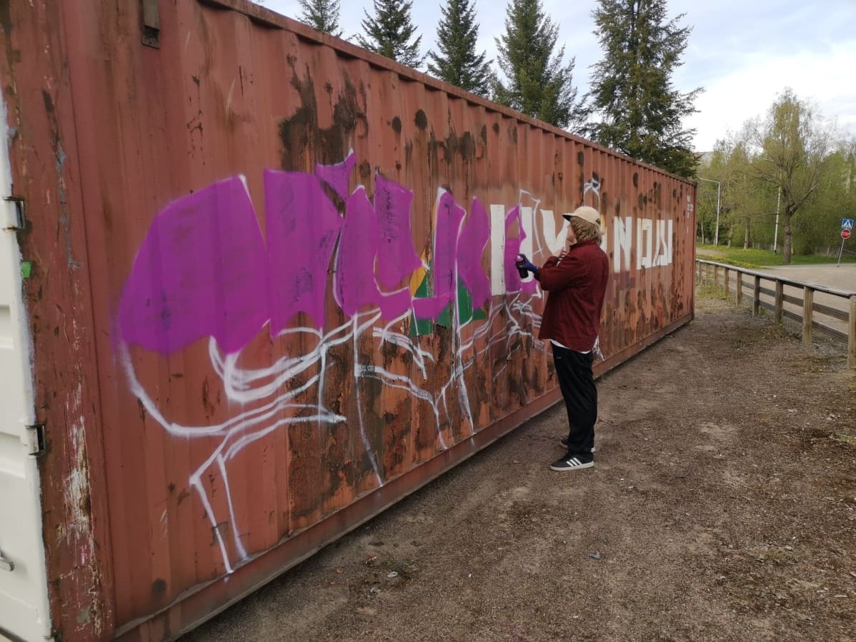 Mies suihkuttaa maalia merikonttiin