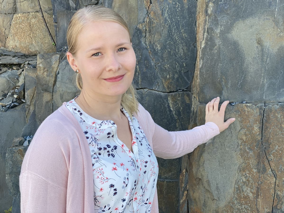 Riina Tervonen seisoo kallion edessä työpaikkansa parkkipaikalla.