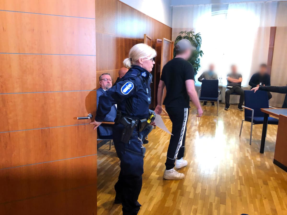 Poliisi tuo murhasta syytettyä uhrin poikaa oikeussaliin Tampereen oikeussalissa.