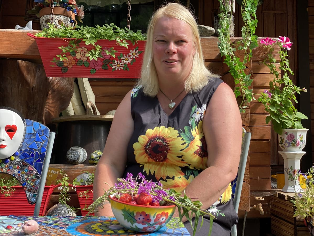 Marjut Kauppinen istuu ulkona mökin edessä.