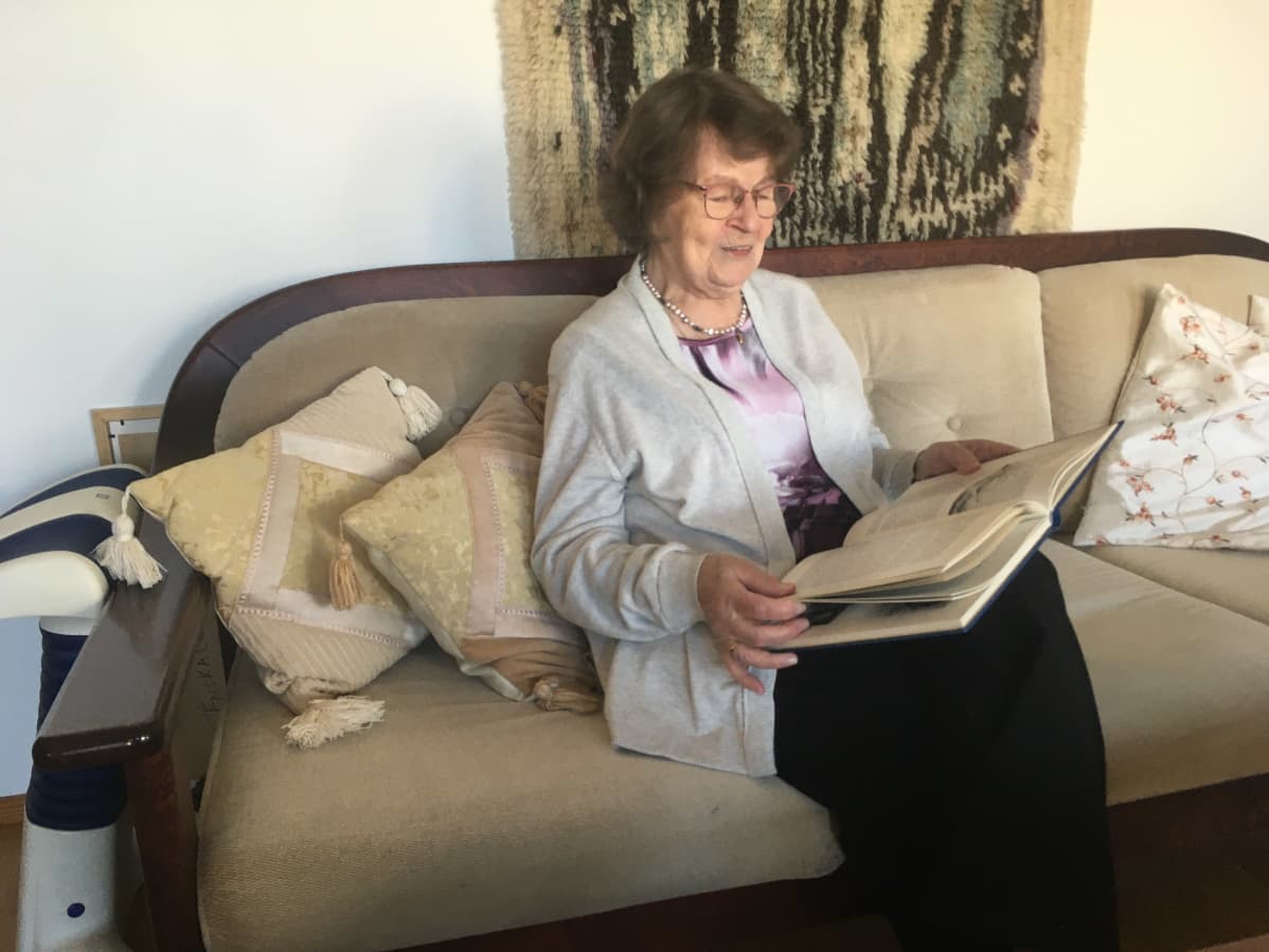 eeva-marja tinkanen istuu sohvalla avonainen kirja käsissään