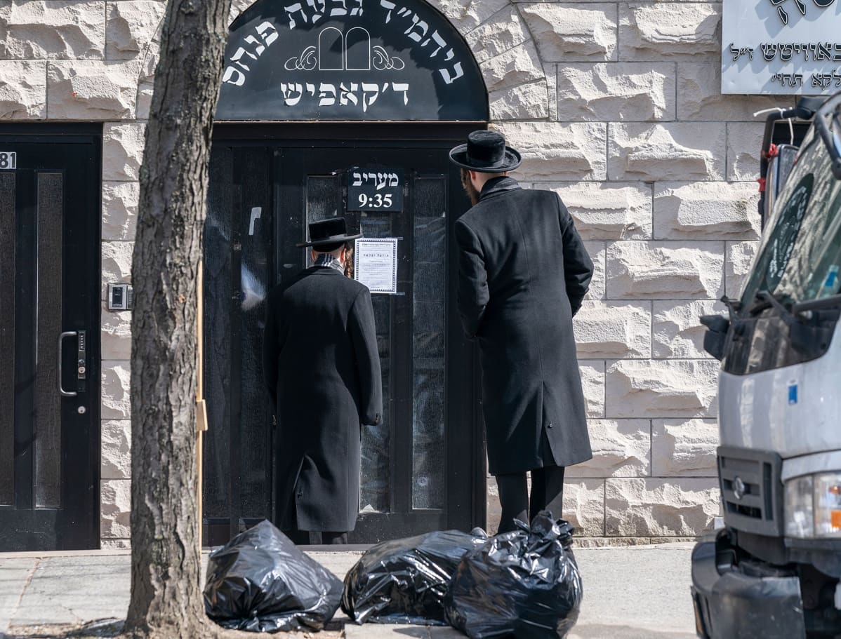 Hasidimiehet lukevat ilmoitusta koronavirksen sulkemasta synagogan ovesta.