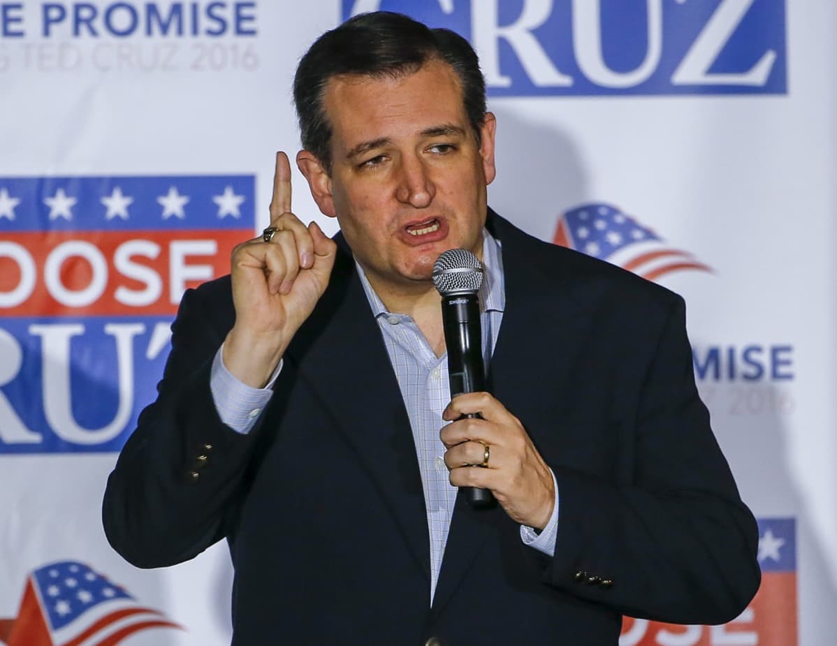 Ted Cruz puhuu mikrofoniin osoittaen oikean kätensä etusormella ylöspäin. Hänellä on tumma puku, kauluspaita mutta ei kravattia. Taustalla on Cruzin kampanjajulistetta.