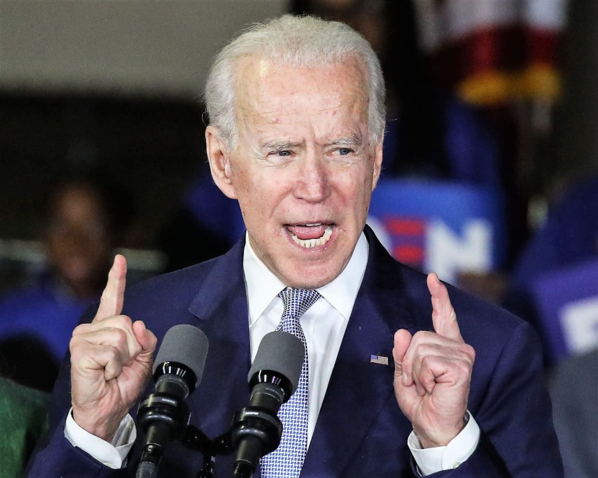 Biden puhuu osoittaen sormillaan ylöspäin. Hänellä on tummansininen puku. Taustalla näkyy Bidenin kannattajia.