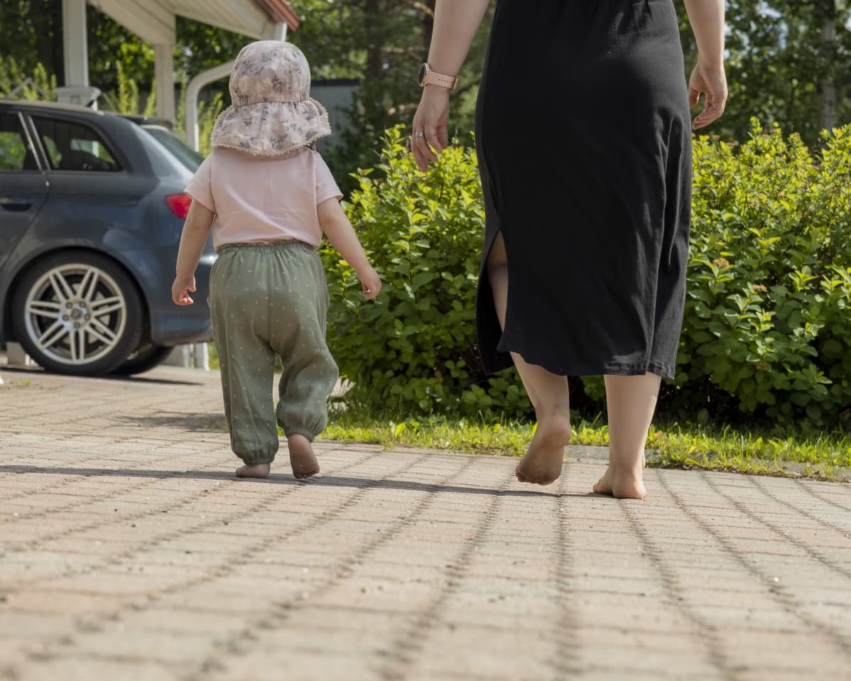 Äiti ja lapsi kävelevät paljain jaloin pihamaalla
