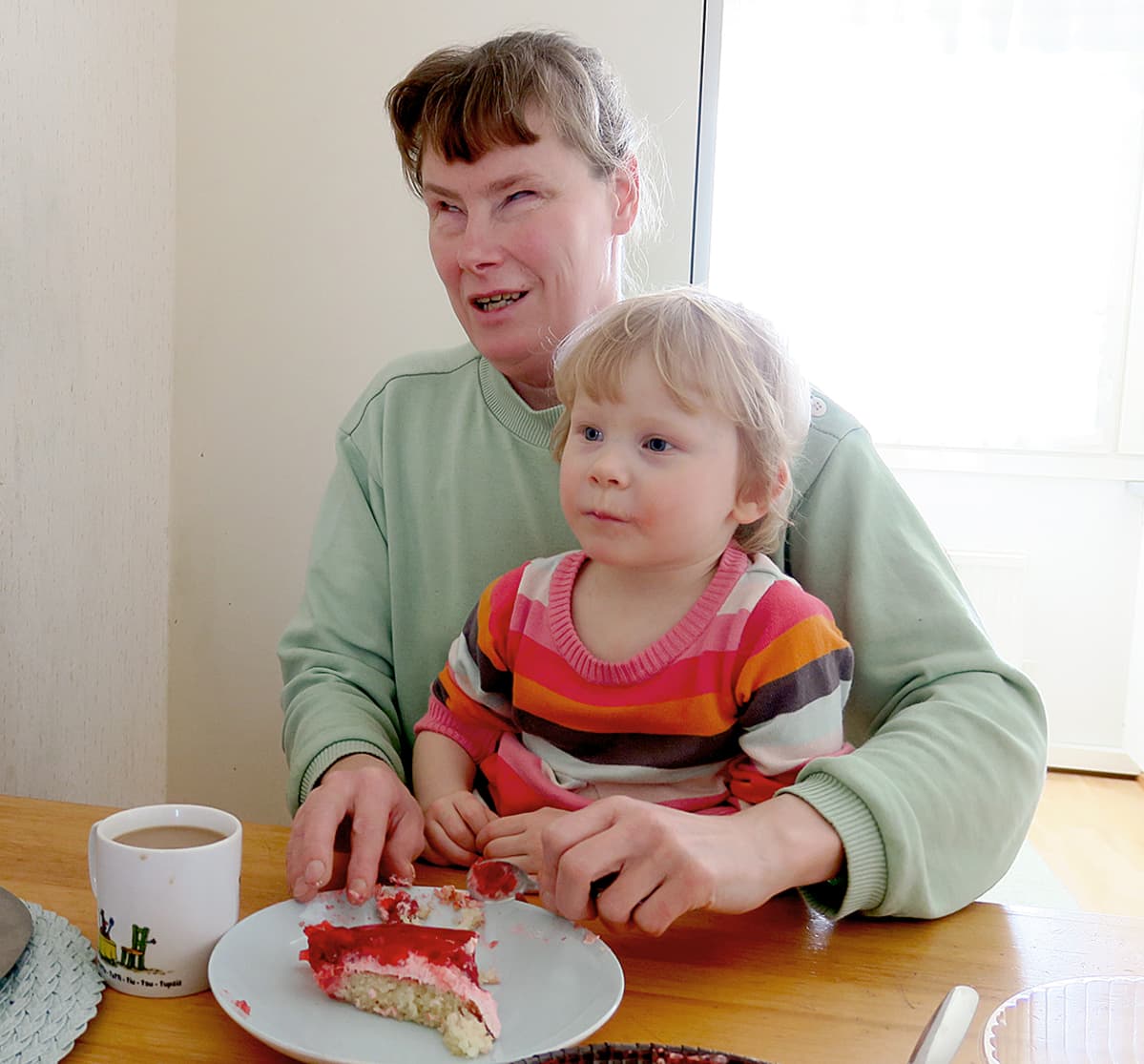 Nainen tyttö sylissään keittiön pöydän ääressä