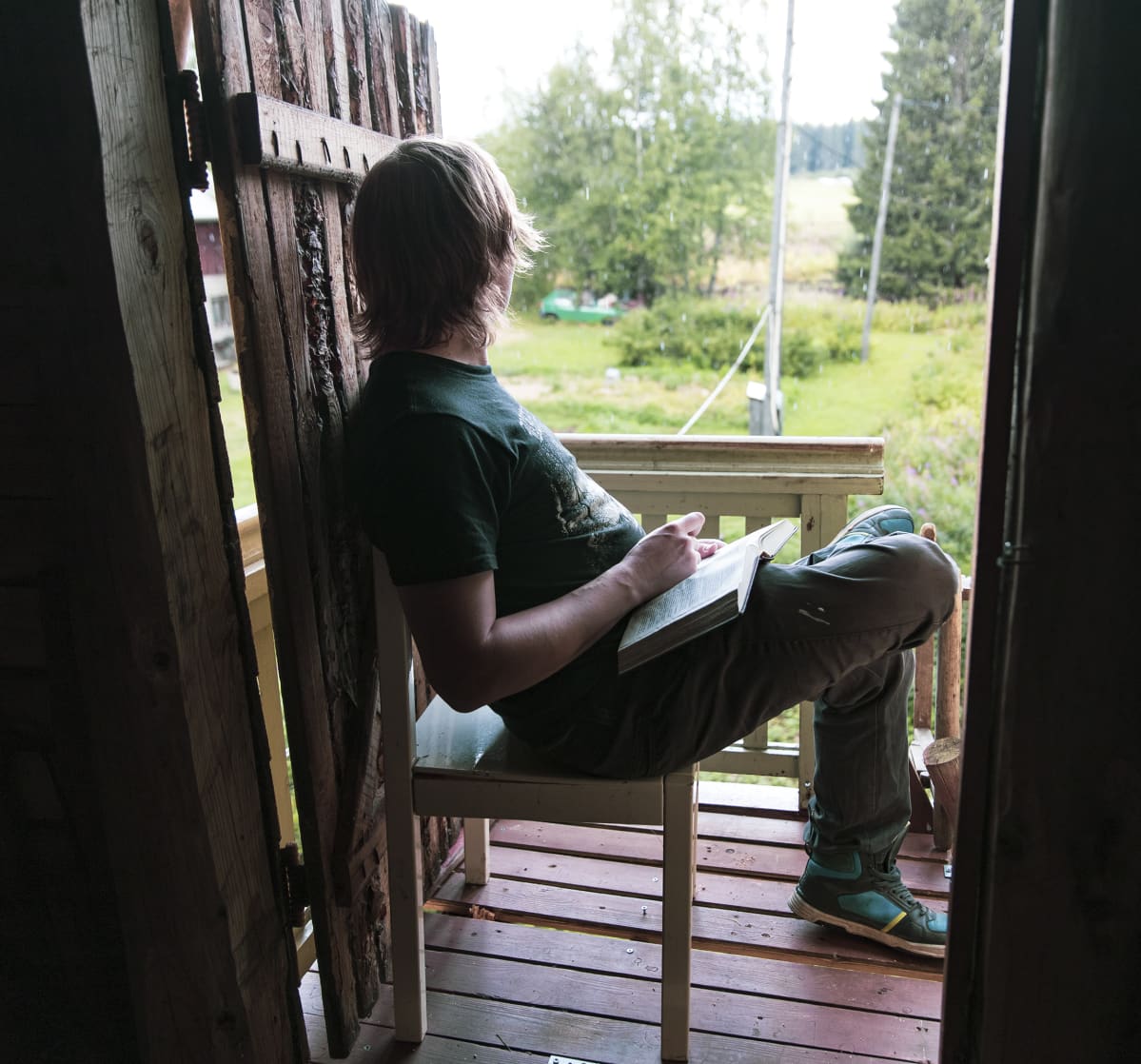 Lauri Ainala istuu parvekkeella ja katsoo maalaismaisemaa.