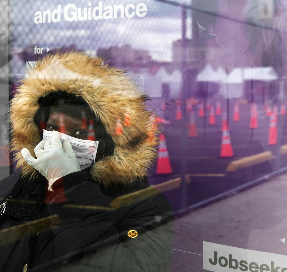 Hengityssuojaimeen pukeutunut nainen odottaa linja-autoa bussipysäkillä New Yorkissa.