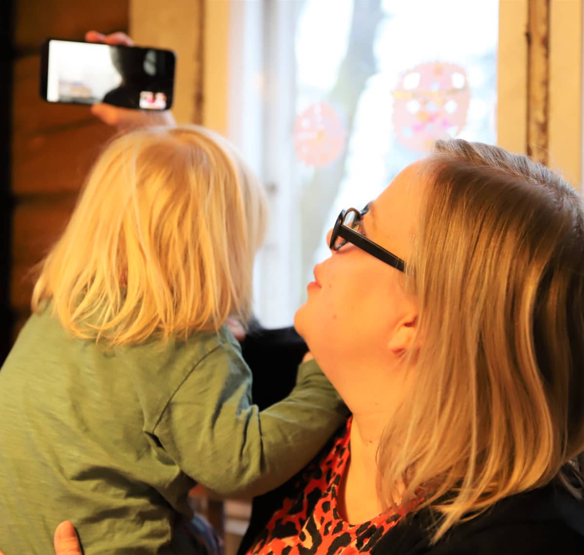 Äidin sylissä istuva pikkupoika katsoo hahmoa älypuhelimen ruudulla