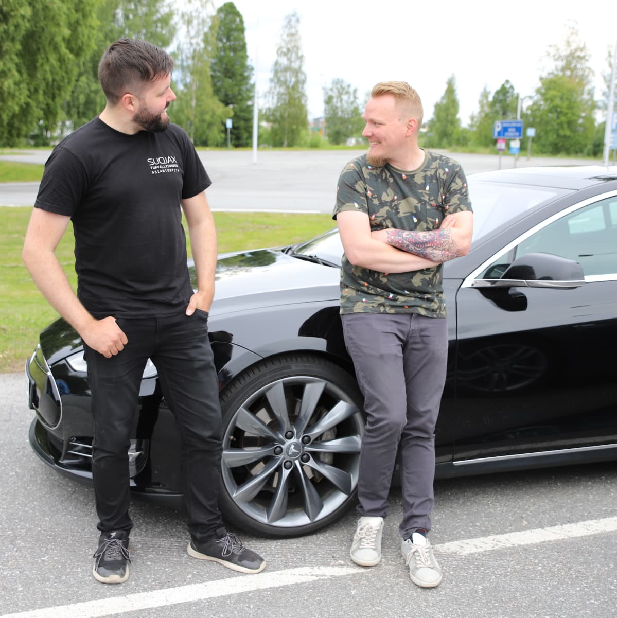 Kaksi miestä nojailee autoon ja katsoo toisiinsa