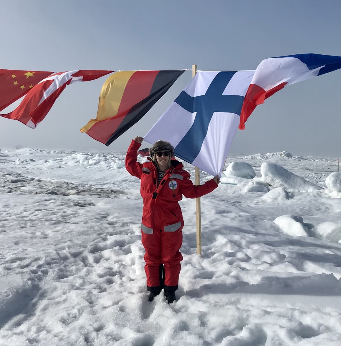 Tuija Jokinen pitelee Suomen lipun reunaa. Narulla riippuvat tutkimushankkeen osanottajamaiden liput.