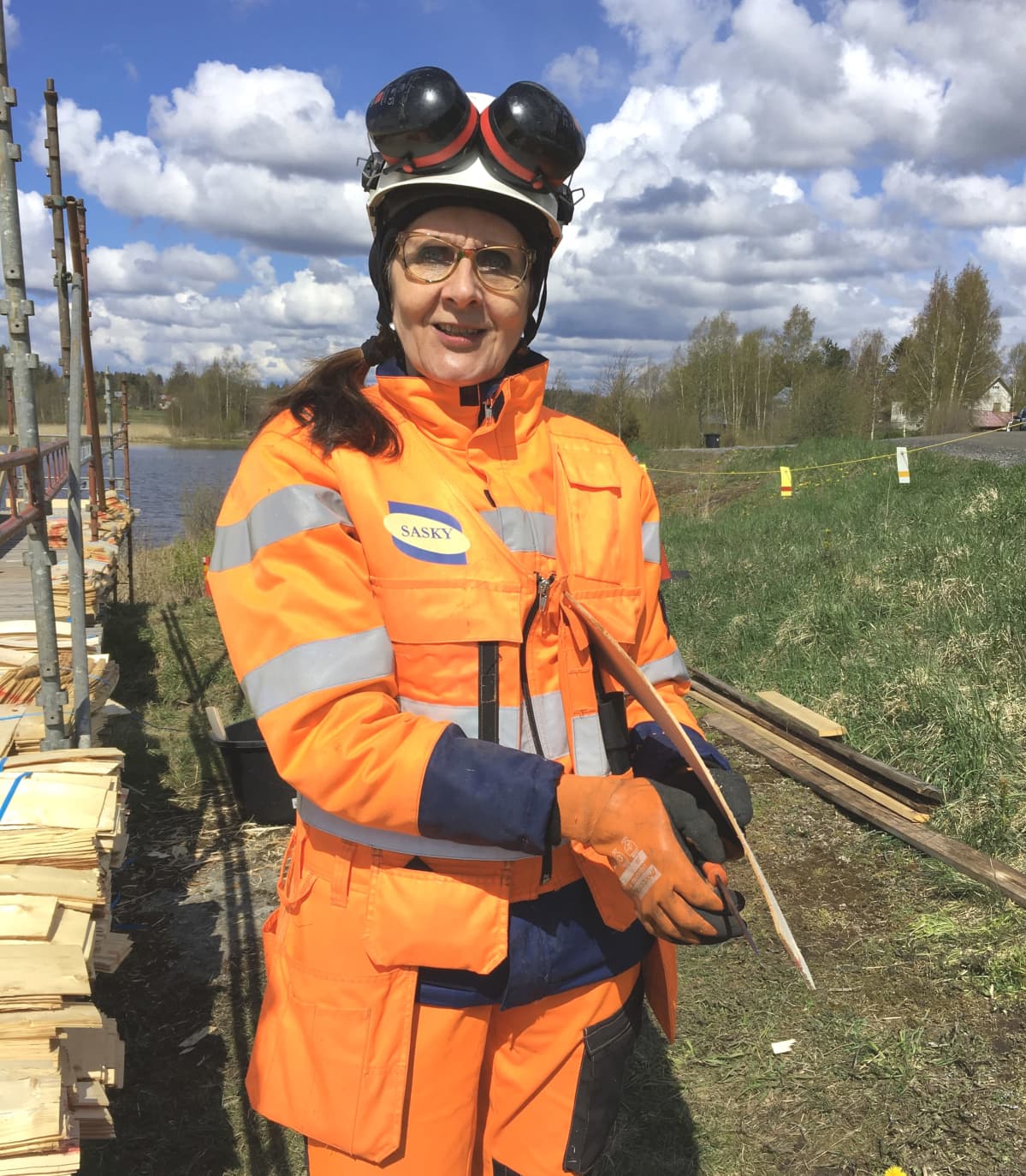 Lehtori Eija Hesso viimeistelee puukolla päreitä työvaatteissa ja kypärä päässä.