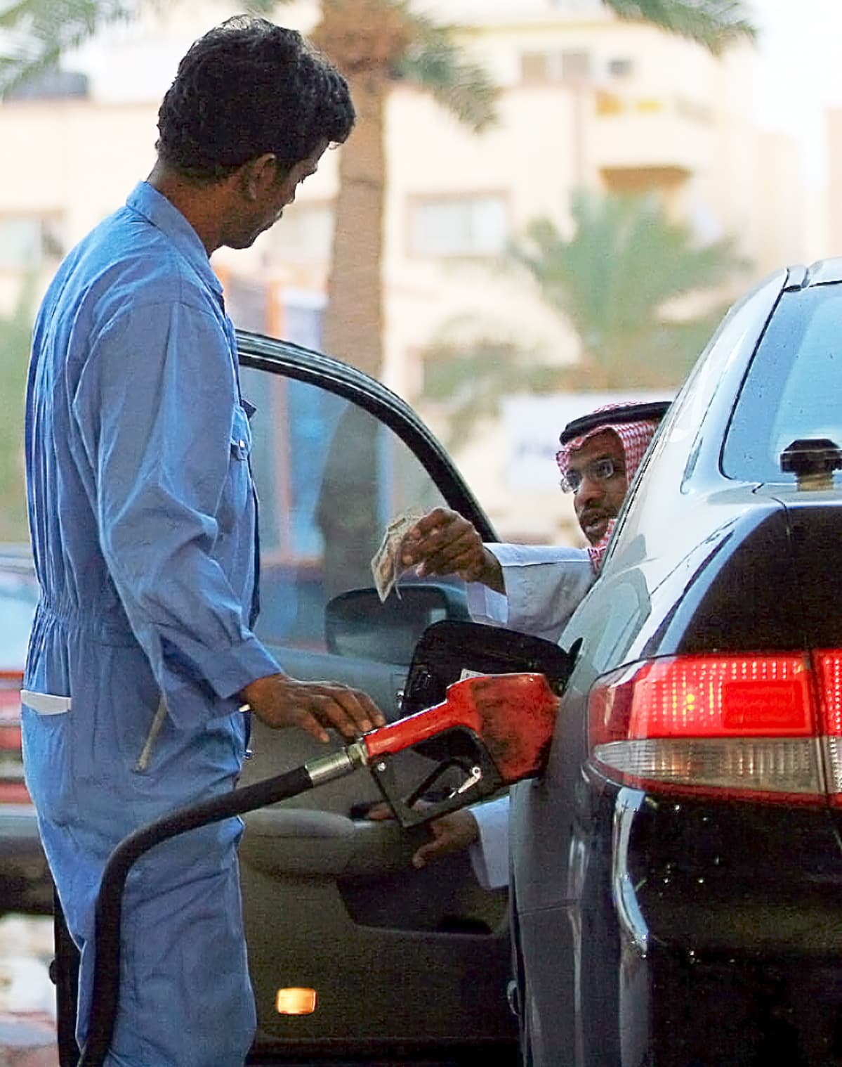 Saudimies maksaa huoltoasemalla autonsa tankkauksesta.
