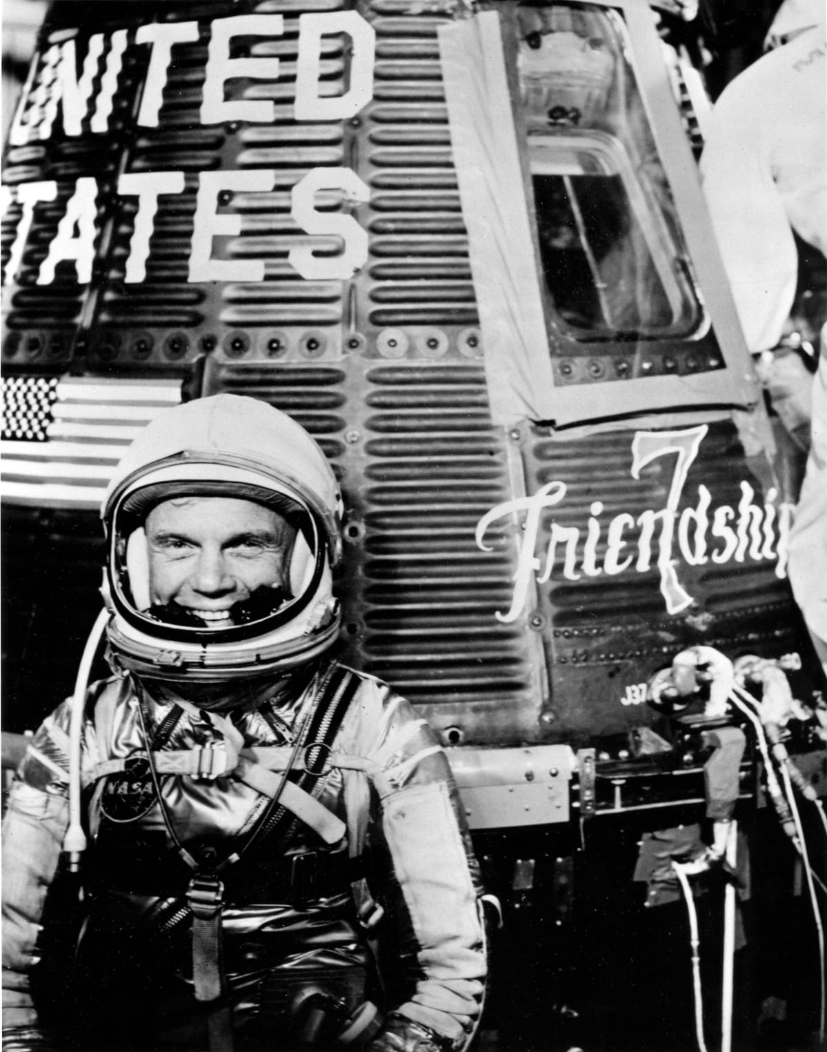 Mustavalkoinen kuva, John Glenn hymyilee avaruskypärä päässään.