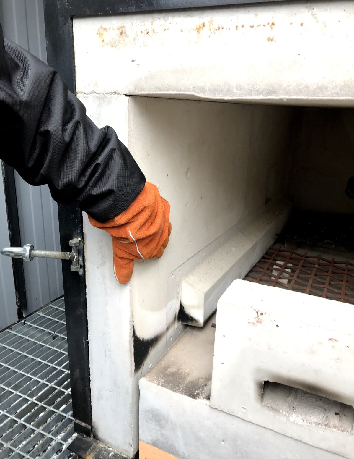 Mies kokeilee käsine kädessä polttouunin seinämän lämpötilaa esilämmityksen jälkeen.