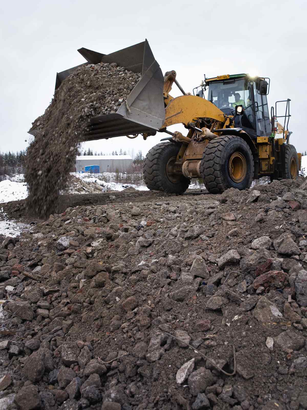 Kauhakuormaaja levittää betonimursketta tiepohjaan.