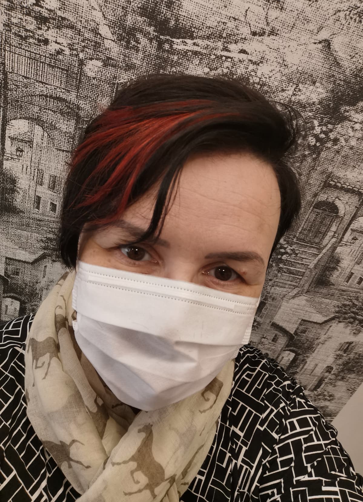 Etukameralla otettu selfie, jossa nainen katsoo kameraan kasvomaski naamalla.
