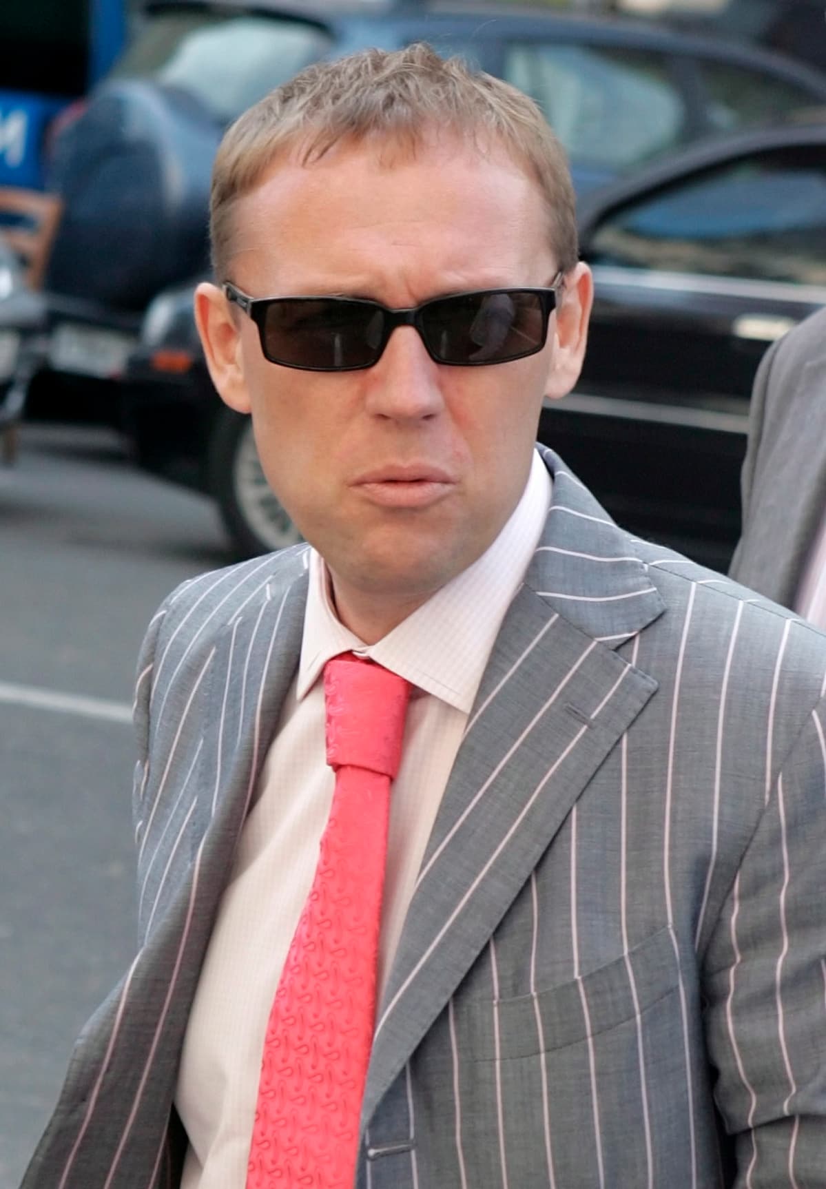 Andrei Lugovoi mustat lasit pääsään, raidallisessa harmaassa puvussa, vaaleanpunainen kravatti kaulassaan.
