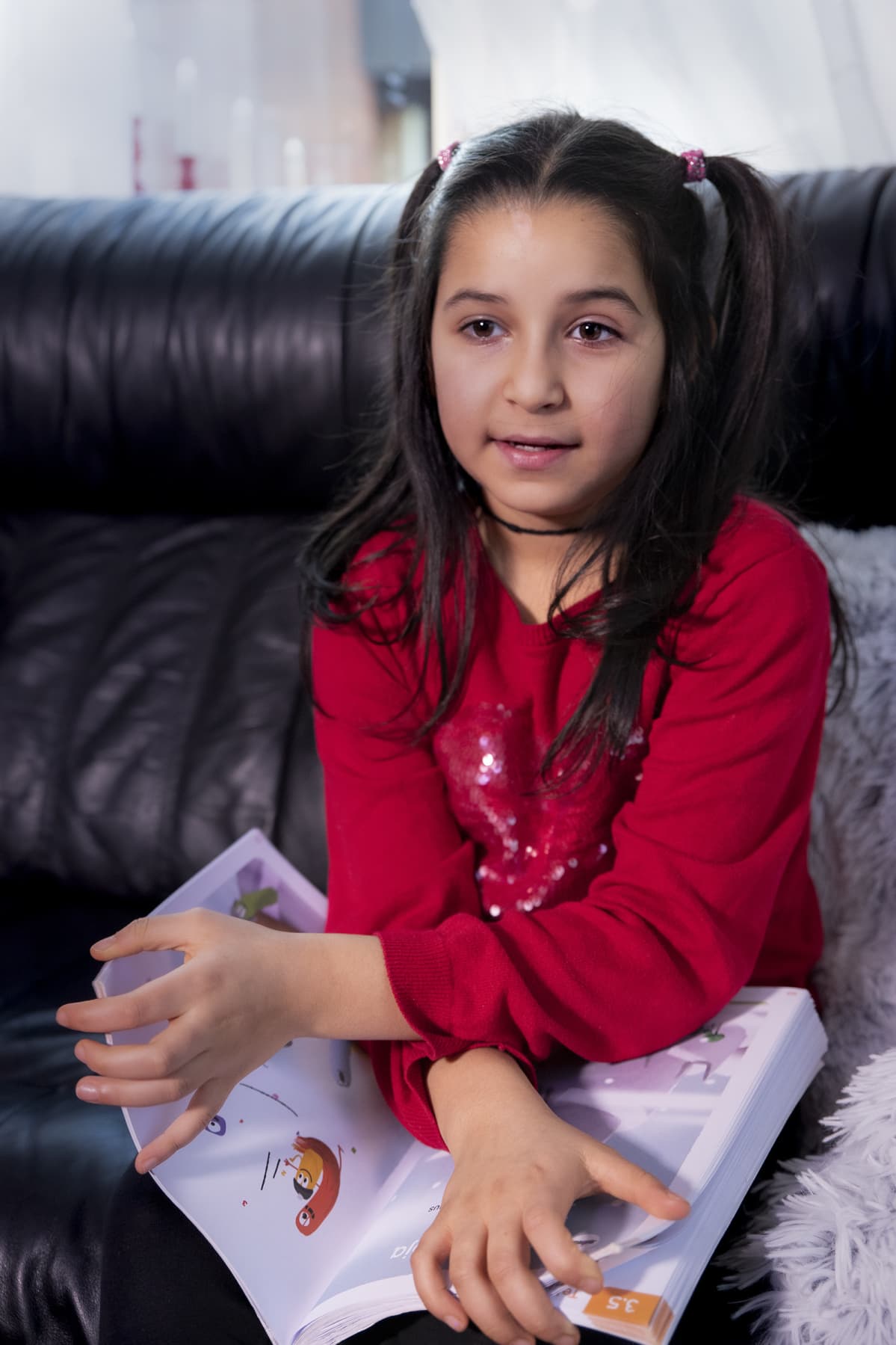 Husna Azimi istuu kotona sohvalla koulukirja kädessä.