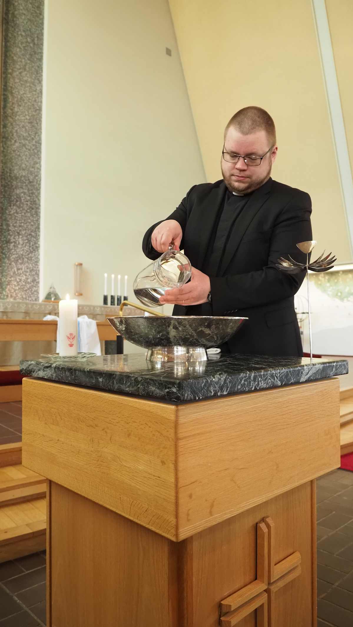 Kuvassa on seurakuntapastori, joka laskee vettä kastemaljaan.
