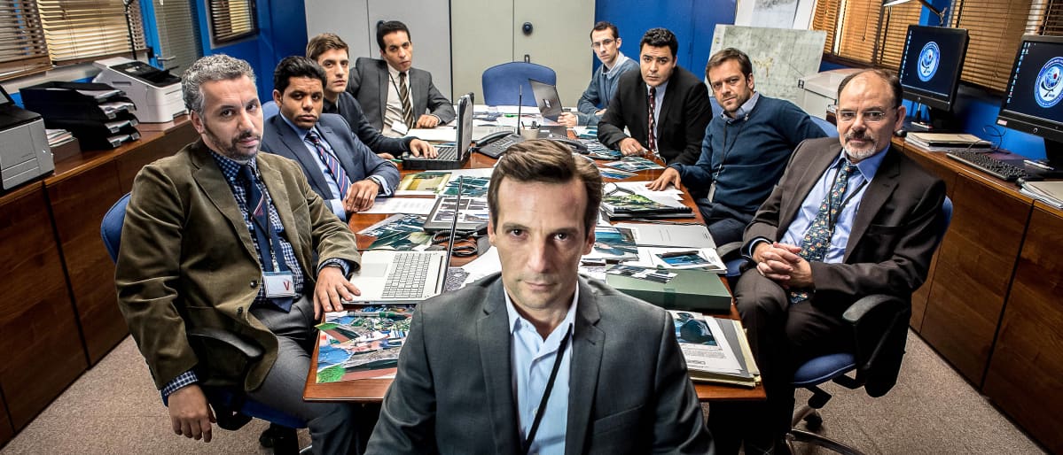 Le bureau, vakoojaverkosto -sarjan miehet istuvat pöydän äärellä ja katsovat kameraan.