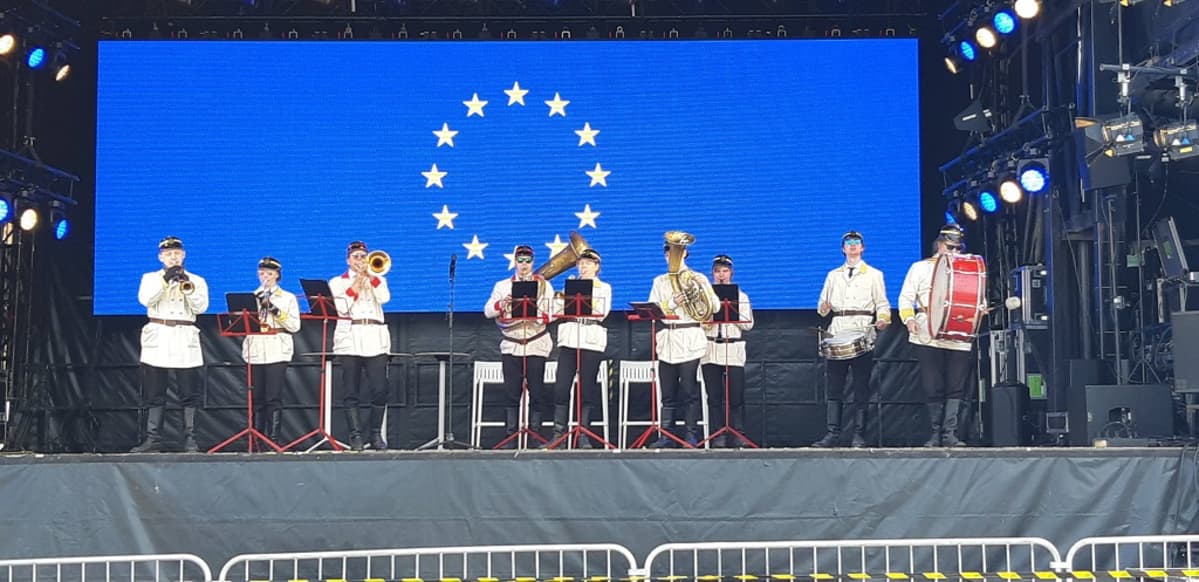 Kuvassa torvisoittokunta esiintymässä Helsingin Narinkkatorilla. Taustalla EU:n lippu.