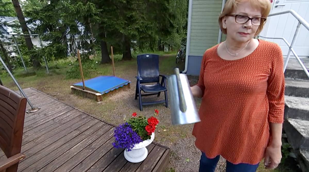 Nainen kastelee kukkia omakotitalonsa pihalla.