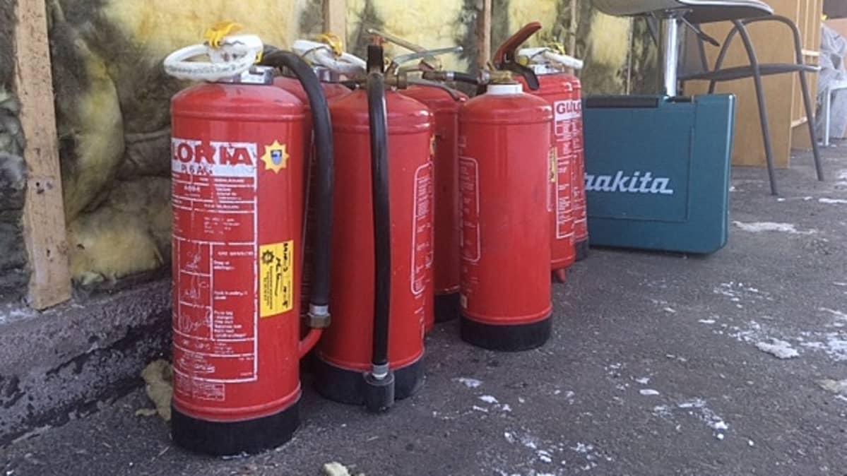 pelastuslaitoksen sammutuspulloja ja työkaluja kerrostalon seinustalla