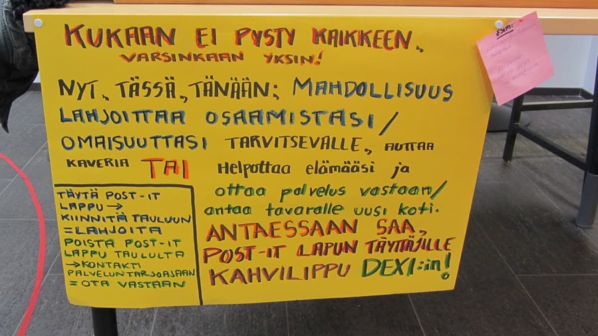 Keltainen tekstikyltti teipattuna pöydän reunaan.