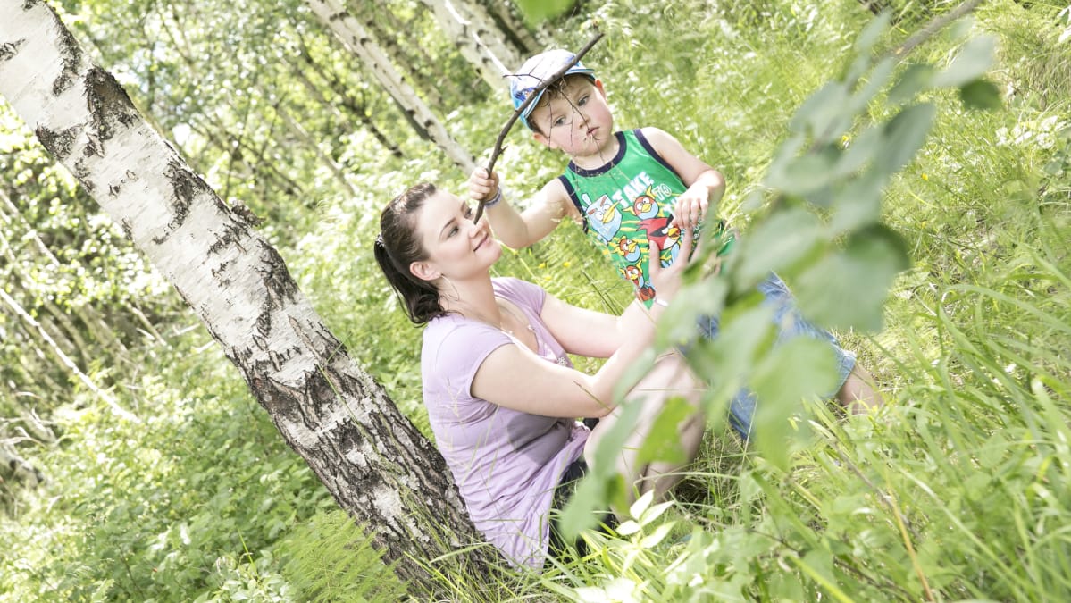 Hanna Pahlsten ja lapsi ihmettelevät oksaa kesäisessä metsässä