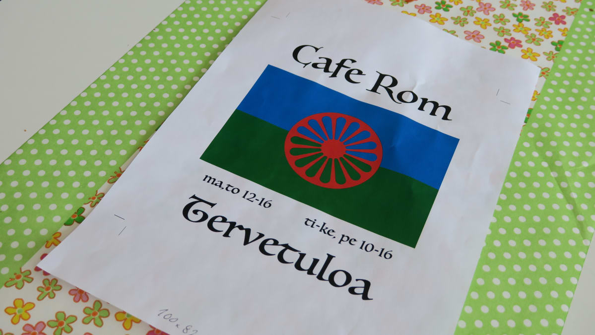 A4-mainoslappu pöydällä. Cafe Rom romanikahvilan mainoksessa romanien lippu.