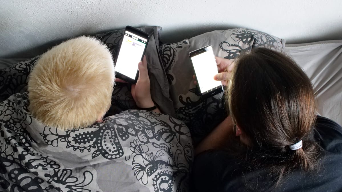 Pariskunta makaa sängyssä puhelimet käsissä.