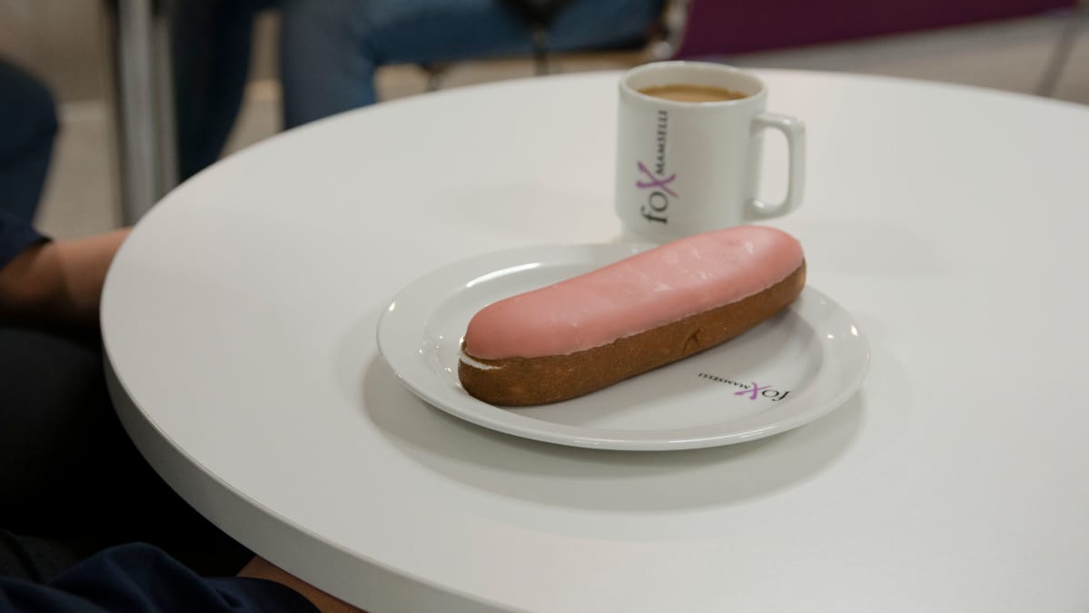 Berliininmunkki ja kahvikuppi koulun ruokalan pöydällä.