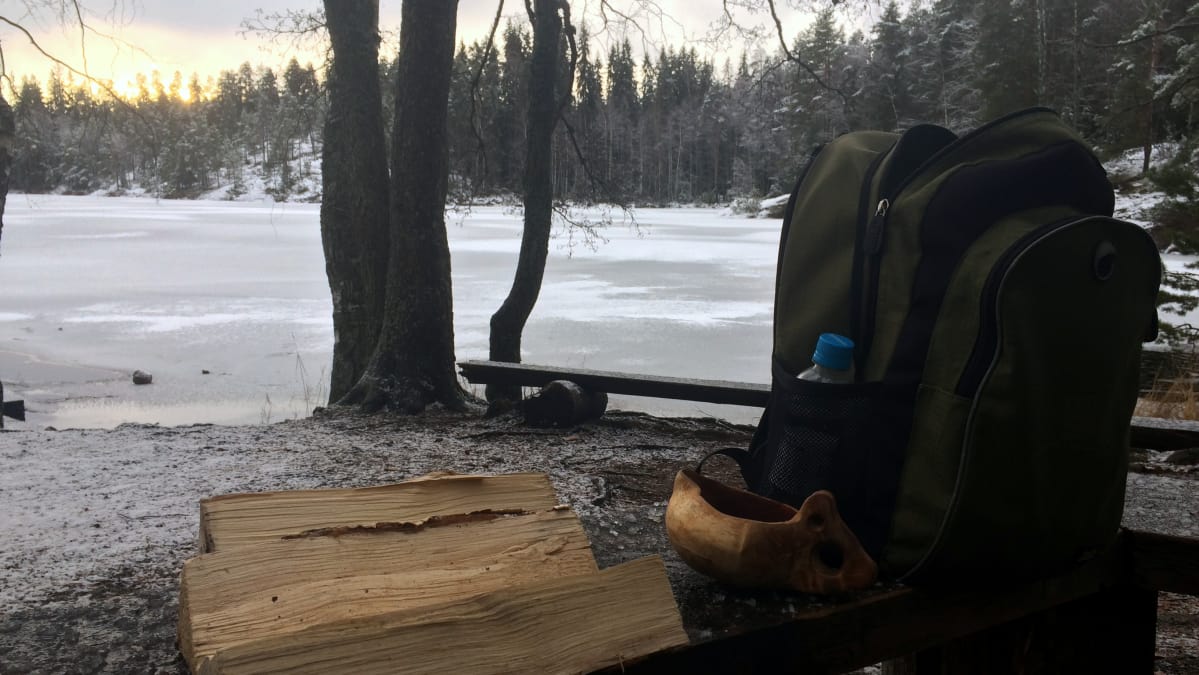 Polttopuut, kuksa ja reppu nuotiopaikan penkillä.