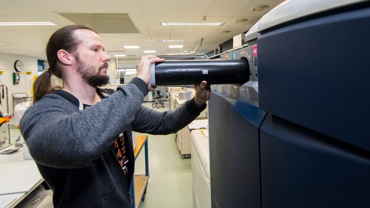 Painotalon työntekijä vaihtaa digitaalipainon värikasettia.