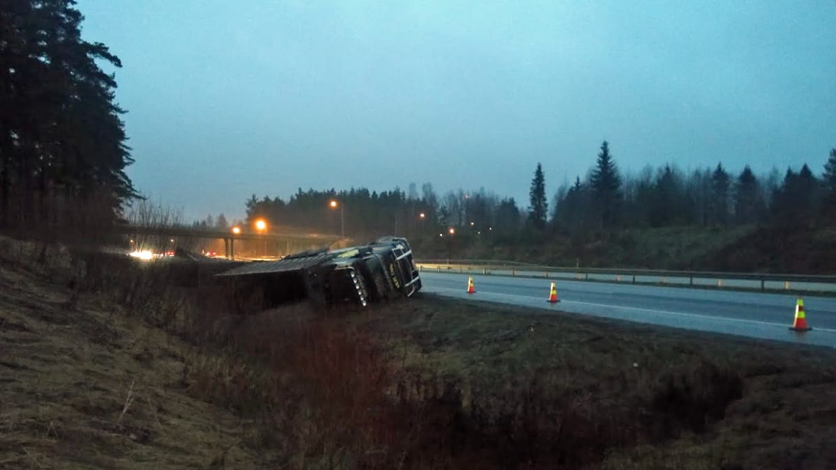 Täysperävaunullinen kuorma-auto makaa kyljellään moottoritien sivussa.