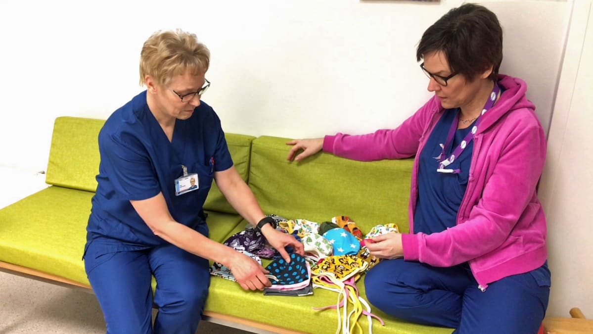 Osastonhoitaja Tiina Kemppainen ja kätilö Mary Viander-Laine katsovat pipoja sohvalla
